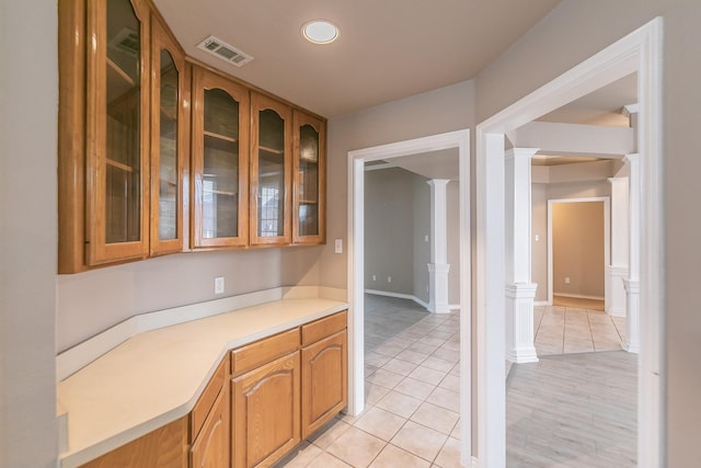 kitchen with decorative columns, visible vents, brown cabinetry, glass insert cabinets, and light countertops