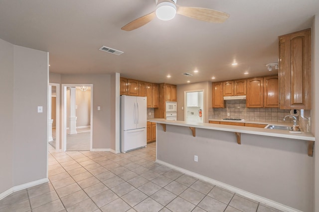 kitchen featuring white appliances, a breakfast bar area, a peninsula, light countertops, and a sink