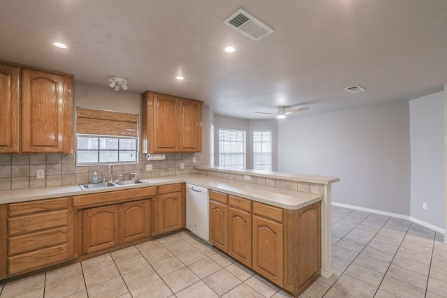 kitchen featuring white dishwasher, a peninsula, a sink, visible vents, and light countertops