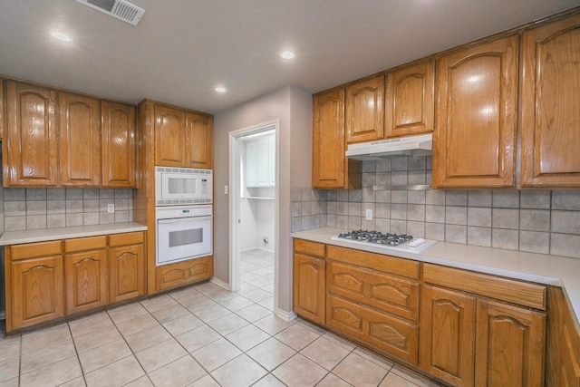 kitchen featuring light countertops, white appliances, brown cabinets, and under cabinet range hood