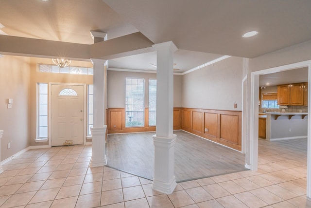 foyer entrance with wainscoting, ornamental molding, light tile patterned flooring, and decorative columns