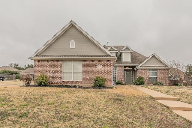 view of front of house featuring brick siding, fence, and a front lawn