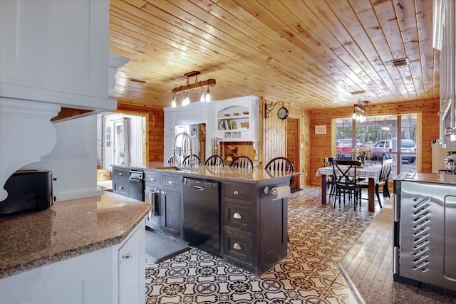 kitchen featuring wooden walls, decorative light fixtures, black dishwasher, sink, and light stone countertops