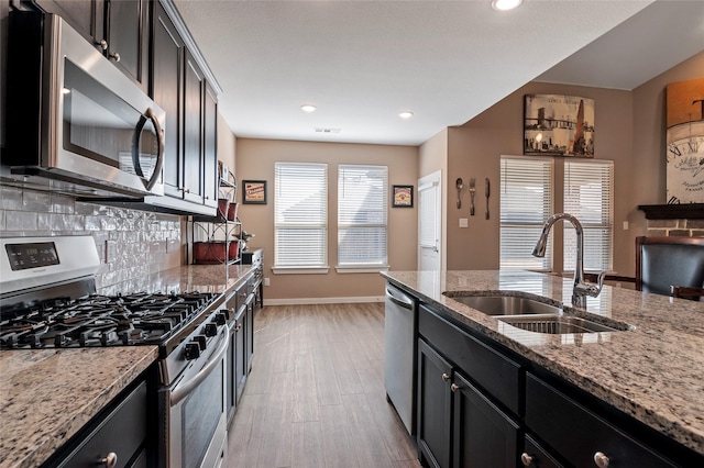 kitchen featuring sink, stainless steel appliances, light stone counters, tasteful backsplash, and light wood-type flooring