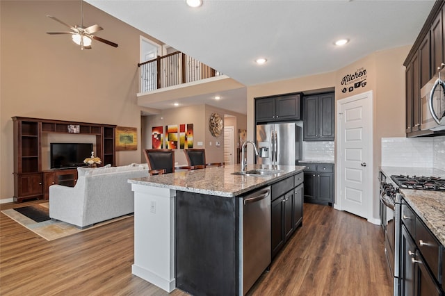 kitchen with hardwood / wood-style flooring, appliances with stainless steel finishes, light stone countertops, and a kitchen island with sink