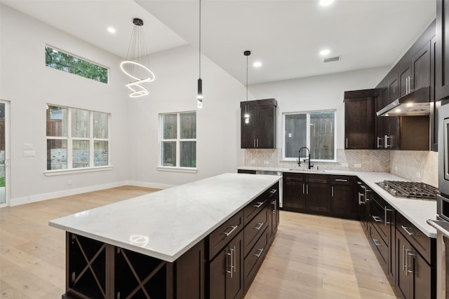 kitchen with a kitchen island, tasteful backsplash, stainless steel gas stovetop, hanging light fixtures, and light hardwood / wood-style floors