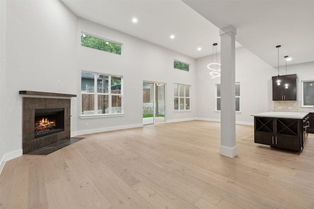 unfurnished living room featuring a fireplace, a towering ceiling, light hardwood / wood-style flooring, and decorative columns