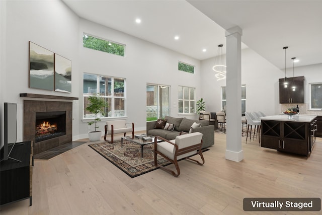 living room with a towering ceiling, light hardwood / wood-style flooring, a tile fireplace, and decorative columns