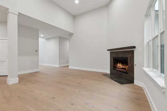 unfurnished living room featuring a fireplace, light hardwood / wood-style flooring, and a high ceiling