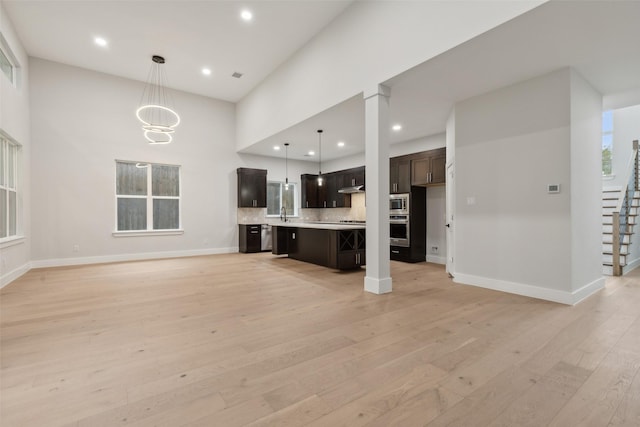 unfurnished living room with a chandelier, sink, light hardwood / wood-style flooring, and a high ceiling