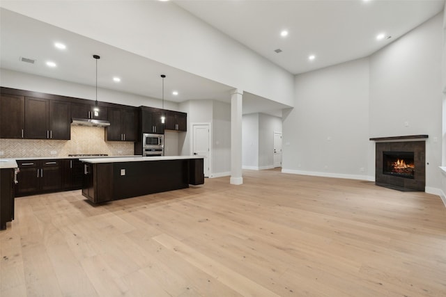 kitchen featuring pendant lighting, light hardwood / wood-style flooring, appliances with stainless steel finishes, a kitchen island, and decorative backsplash