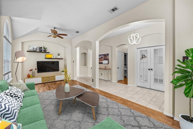 living area with ceiling fan with notable chandelier, wood finished floors, visible vents, and arched walkways