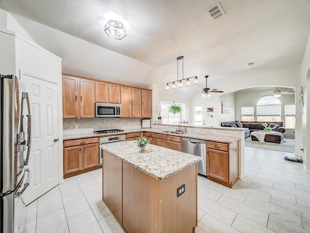 kitchen with decorative light fixtures, sink, a center island, stainless steel appliances, and light stone countertops