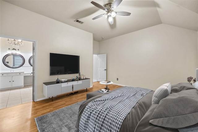 bedroom with lofted ceiling, ceiling fan with notable chandelier, ensuite bath, and light wood-type flooring