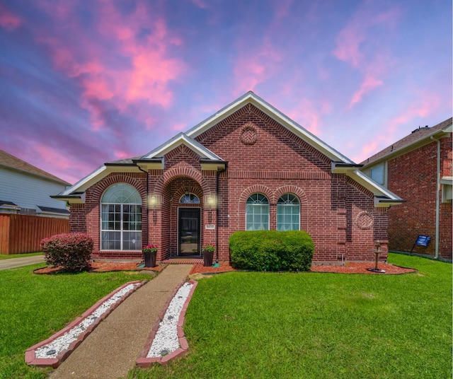 view of front of home featuring brick siding, a lawn, and fence