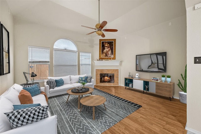 living room with a tiled fireplace, hardwood / wood-style flooring, vaulted ceiling, and ceiling fan