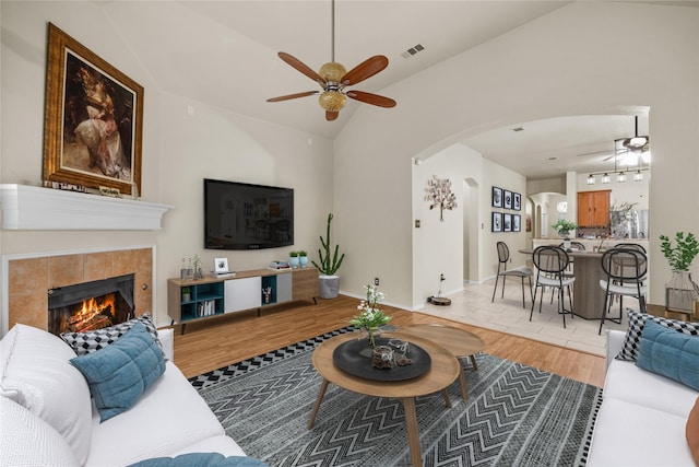 living room featuring vaulted ceiling, ceiling fan, a tiled fireplace, and light hardwood / wood-style floors