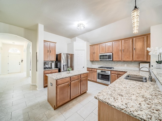 kitchen with sink, decorative light fixtures, a kitchen island, stainless steel appliances, and light stone countertops