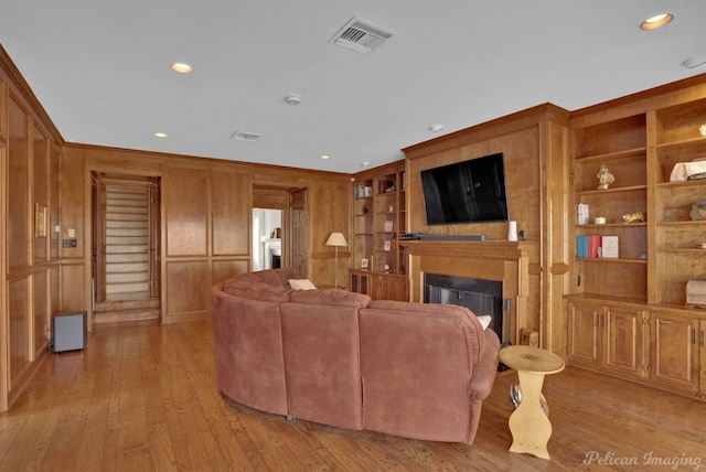 living room with crown molding, wooden walls, built in features, and light hardwood / wood-style floors