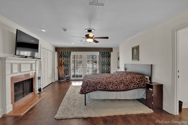 bedroom featuring french doors, ornamental molding, dark hardwood / wood-style floors, ceiling fan, and a fireplace