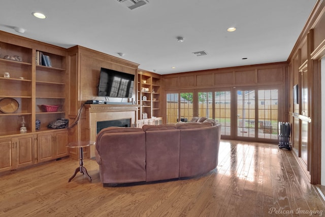 living room with french doors, wooden walls, light hardwood / wood-style floors, and built in features