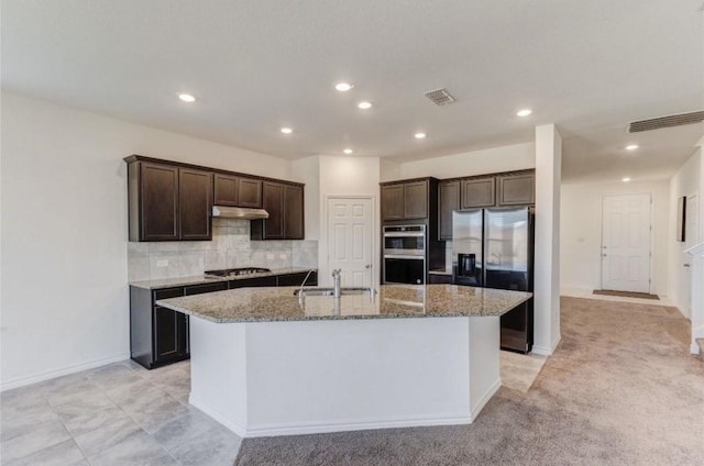 kitchen with visible vents, dark brown cabinets, a center island with sink, light stone counters, and appliances with stainless steel finishes