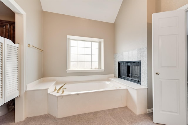 bathroom featuring a tile fireplace, lofted ceiling, and a tub to relax in