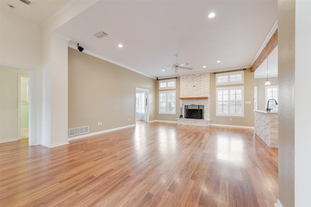 unfurnished living room featuring crown molding, a stone fireplace, light hardwood / wood-style floors, and ceiling fan