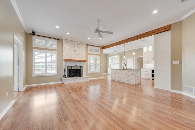 unfurnished living room with sink, a stone fireplace, ornamental molding, and light hardwood / wood-style floors