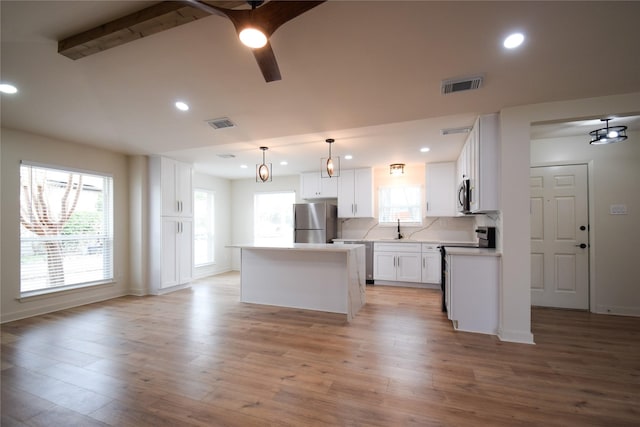 kitchen with sink, white cabinetry, a kitchen island, decorative light fixtures, and stainless steel appliances