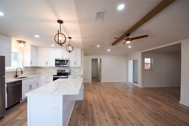 kitchen with appliances with stainless steel finishes, sink, a center island, lofted ceiling with beams, and white cabinets