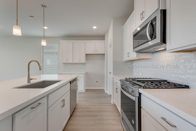 kitchen with decorative light fixtures, sink, white cabinets, stainless steel appliances, and light hardwood / wood-style flooring