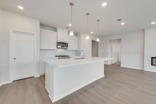 kitchen featuring white cabinetry, an island with sink, stove, and pendant lighting