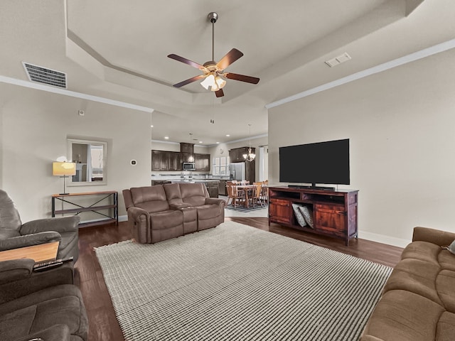 living room featuring dark hardwood / wood-style floors, ceiling fan with notable chandelier, ornamental molding, and a raised ceiling