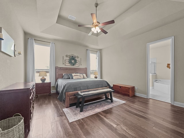 bedroom featuring dark hardwood / wood-style floors, ensuite bath, a tray ceiling, and ceiling fan