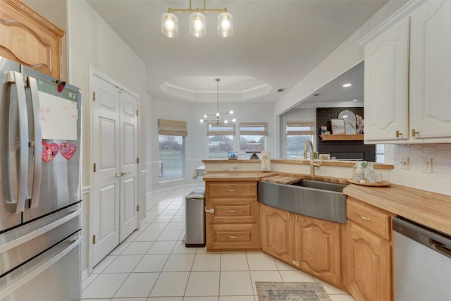 kitchen with sink, tasteful backsplash, decorative light fixtures, appliances with stainless steel finishes, and a raised ceiling