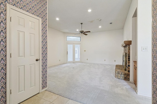 unfurnished living room featuring ceiling fan, a fireplace, light carpet, and a textured ceiling