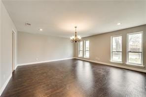 spare room with dark hardwood / wood-style floors and an inviting chandelier