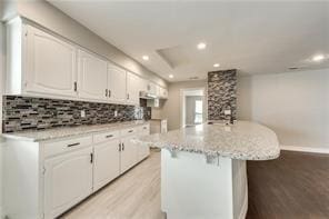 kitchen with light hardwood / wood-style flooring, backsplash, a center island, light stone counters, and white cabinets