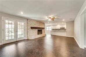 unfurnished living room with a stone fireplace, ceiling fan, and french doors