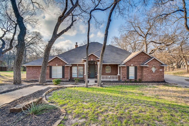 single story home with brick siding, a chimney, a front lawn, and roof with shingles