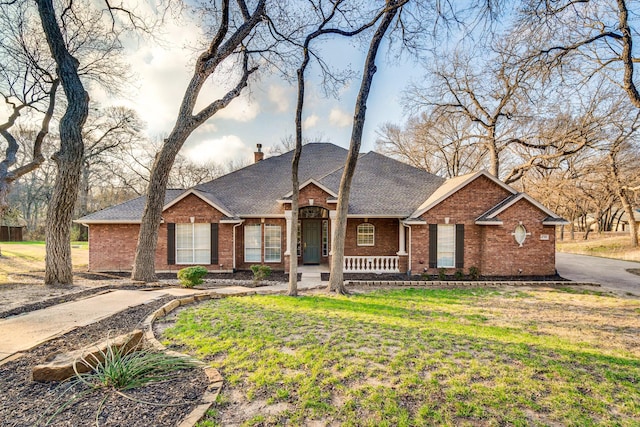 ranch-style home featuring brick siding, a chimney, a front lawn, and a shingled roof