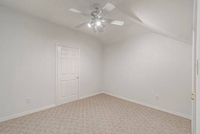 empty room featuring a ceiling fan, light carpet, vaulted ceiling, and baseboards