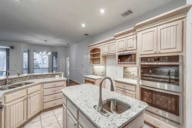 kitchen with stainless steel double oven, a center island with sink, a sink, and light brown cabinetry