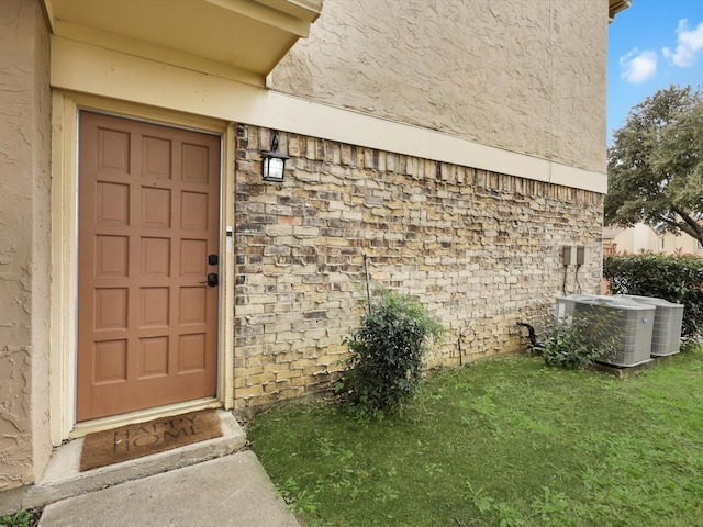 property entrance with central AC unit and a yard