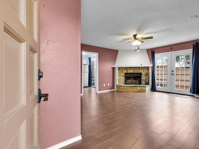 unfurnished living room with hardwood / wood-style floors, ceiling fan, a brick fireplace, a textured ceiling, and french doors