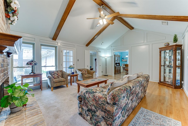 living room featuring high vaulted ceiling, a fireplace, beamed ceiling, ceiling fan, and light wood-type flooring