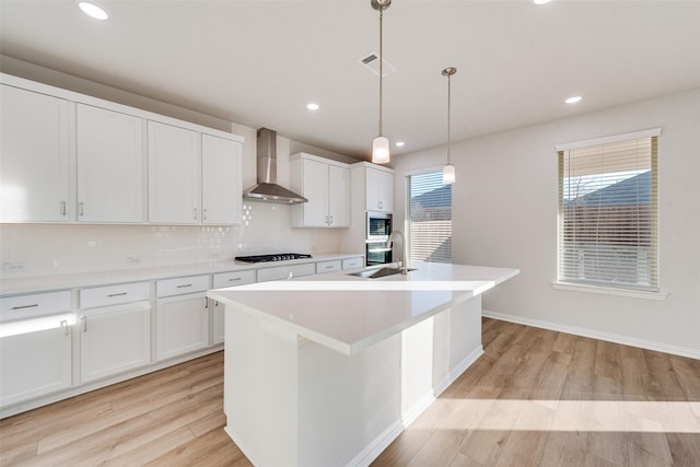 kitchen with wall chimney exhaust hood, sink, a center island with sink, pendant lighting, and white cabinets