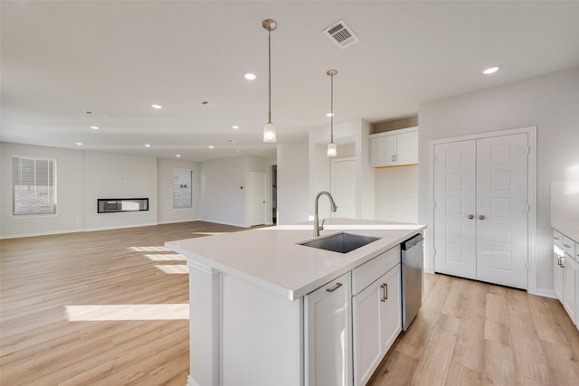 kitchen featuring white cabinetry, sink, stainless steel dishwasher, and an island with sink