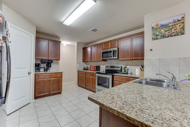 kitchen featuring sink, light tile patterned floors, appliances with stainless steel finishes, backsplash, and a textured ceiling